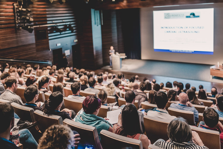 An audience of students listening to a speaker in a lecture hall.