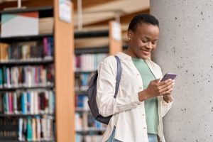 A student smiling at her phone in a library setting.