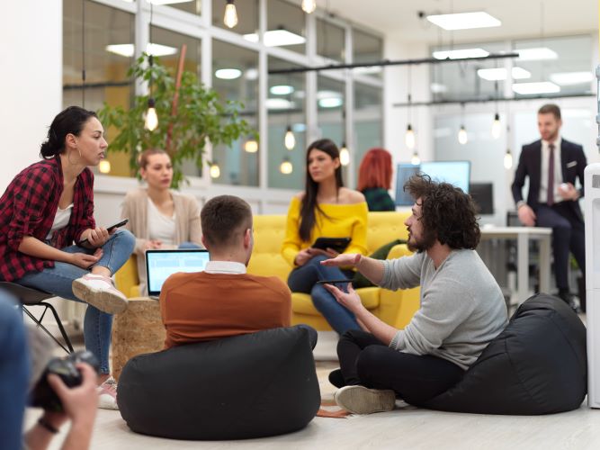 A group of colleagues sit in a circle and engage in a lively discussion in a modern office setting.