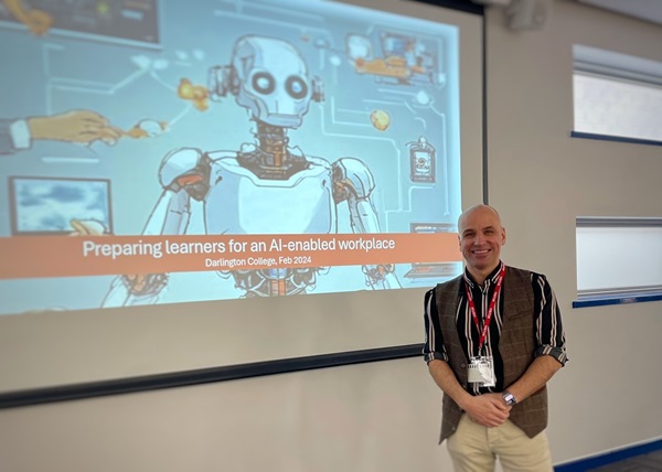 This image shows Scott Hibberson, a Relationship Manager at Jisc and the author of this blog, standing in front of a presentation slide at Darlington College. The slide has the text ‘Preparing learners for an AI-enabled workplace’ as the title and ‘Darlington College, Feb 2024’ as the sub-title. The slide also has an image of a robot. Scott is smiling and looking straight ahead into the camera.