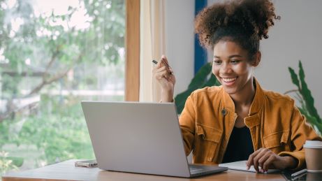 A cheerful student engaging with a laptop at a study desk.