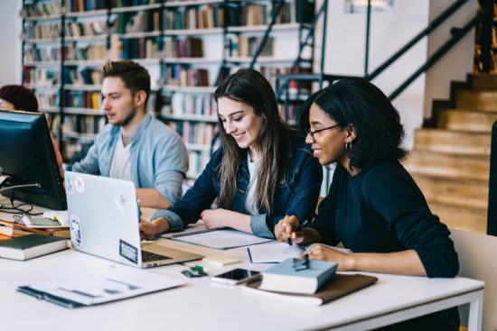 Three people collaborating on a project with laptops in a library.