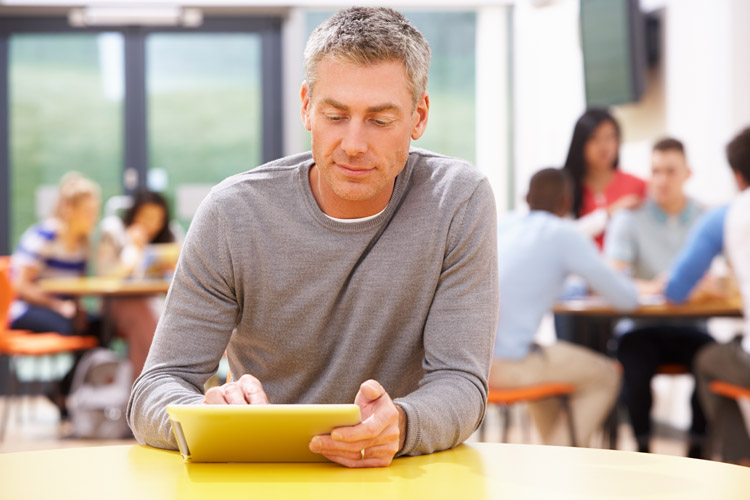 A mature student using a tablet in a busy school cafeteria.