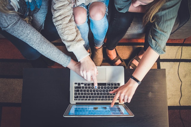 Multiple people pointing at a laptop screen. The image indicates a shared resource.